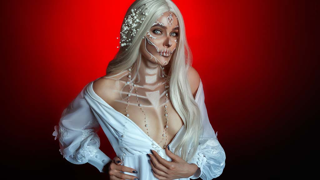 Blonde woman in loose white dress with skeleton makeup.
