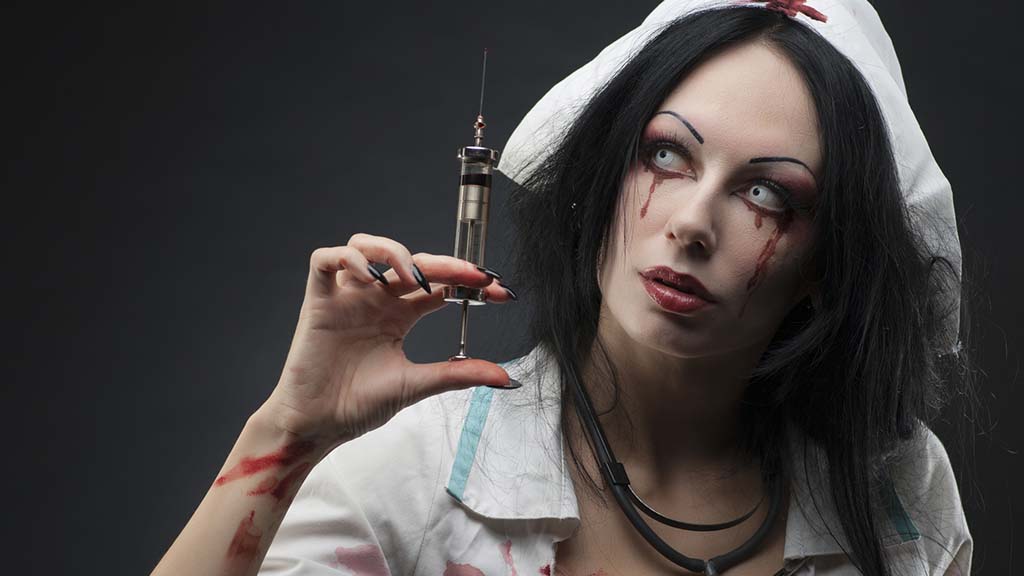 Woman wearing a nurse costume, coloured eye contacts and zombie makeup holding a syringe.