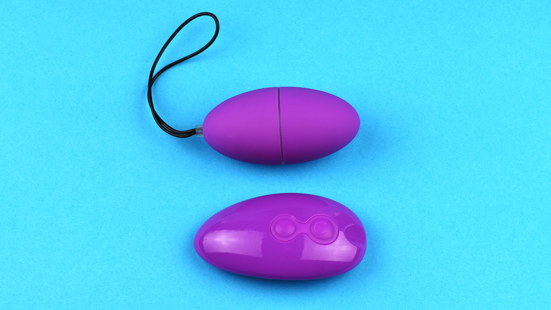 Remote controlled purple egg vibrator next to purple wireless remote. Light turquoise background.