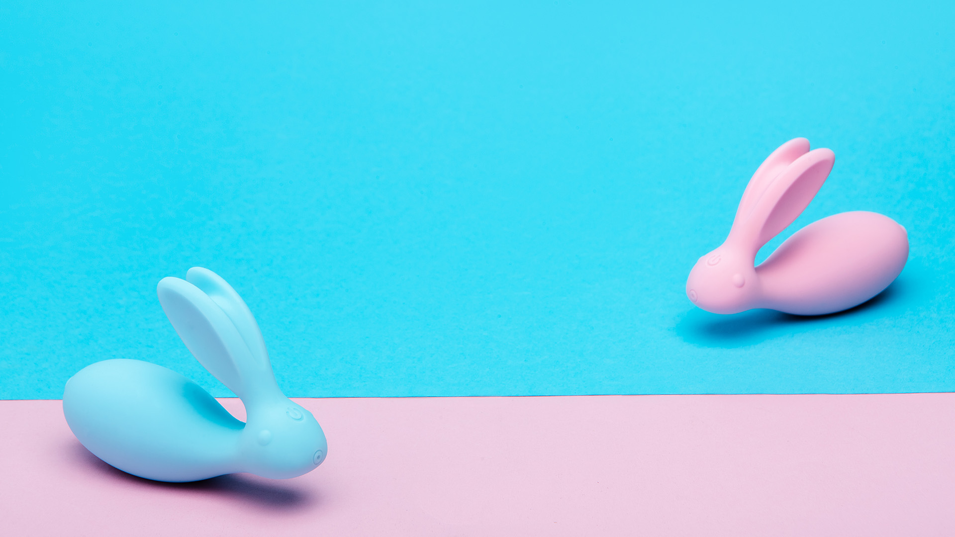 Baby blue and pink colored rabbit shaped vibrators facing each other on baby blue and pink background.