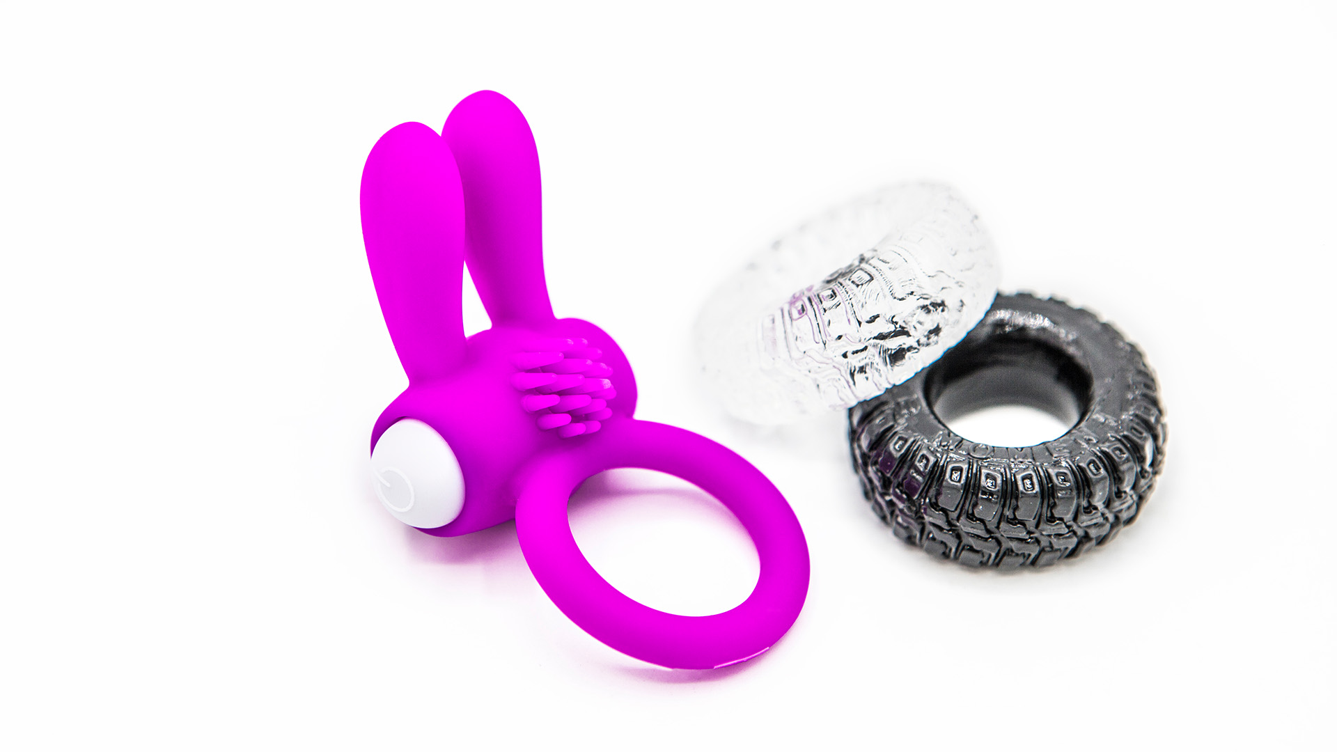 Pink cock ring with bunny ears next to two other cock rings with wheel designs in black and white. White background.