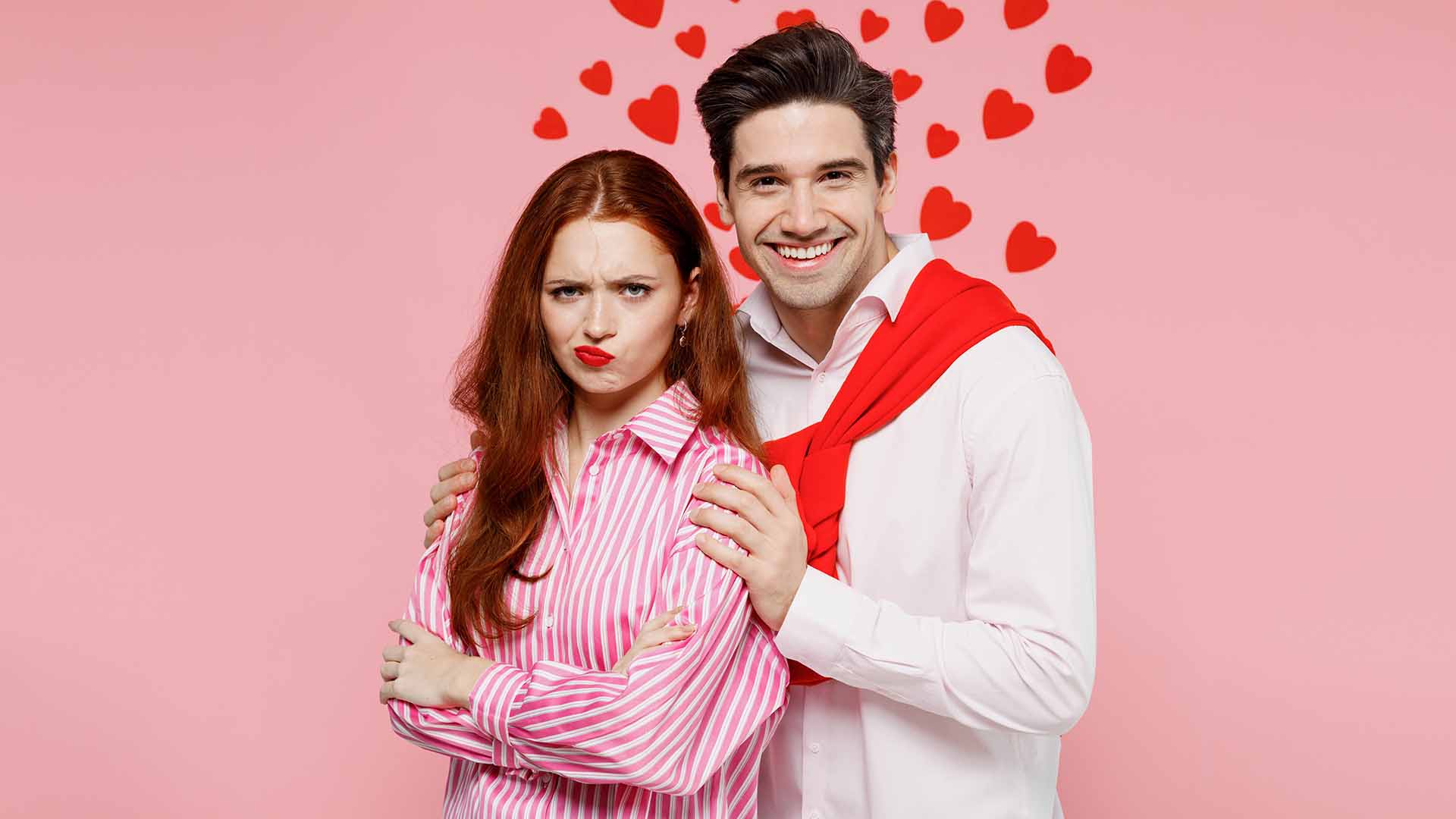 Red-haired woman and brunette man standing close to each other. The woman looks annoyed while the man looks happy.