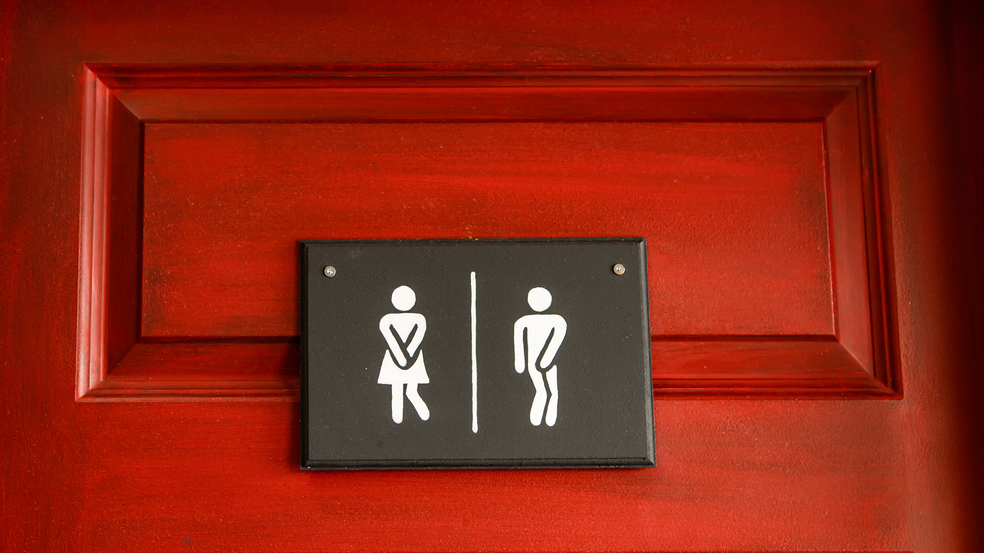 Bathroom sign in front of a red door where the illustrations look like they really need to go to the toilet