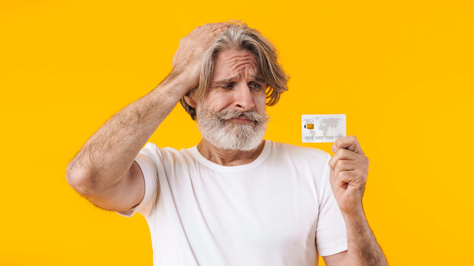 Older man in white short-sleeved shirt holding his visa card and holding his head. Yellow background.