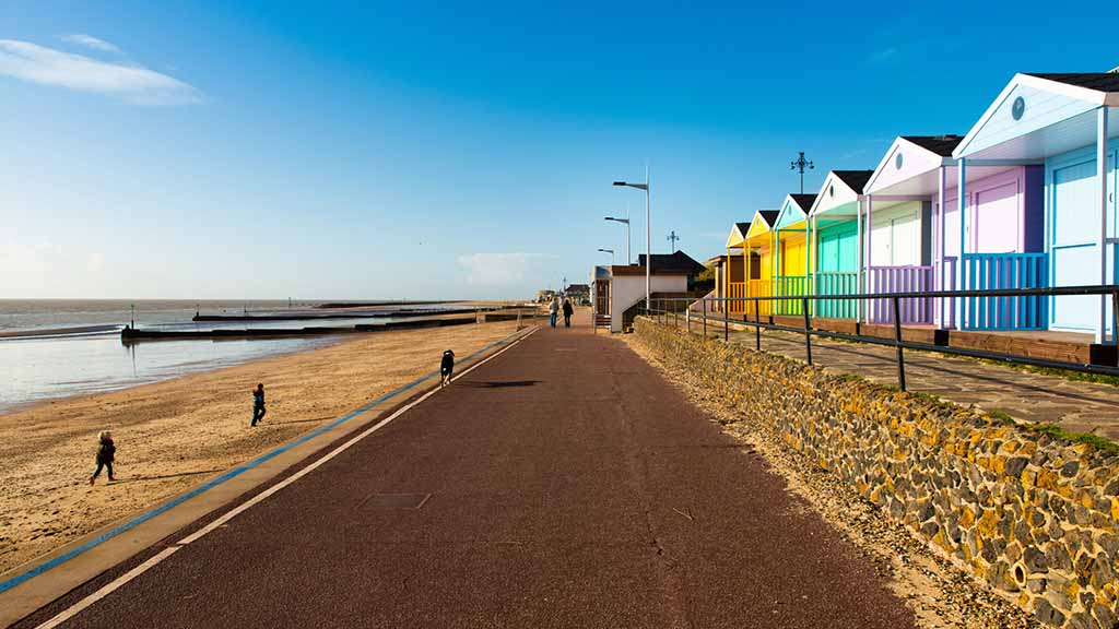 People walking on the beach and going past colorful beach huts in West Mersea