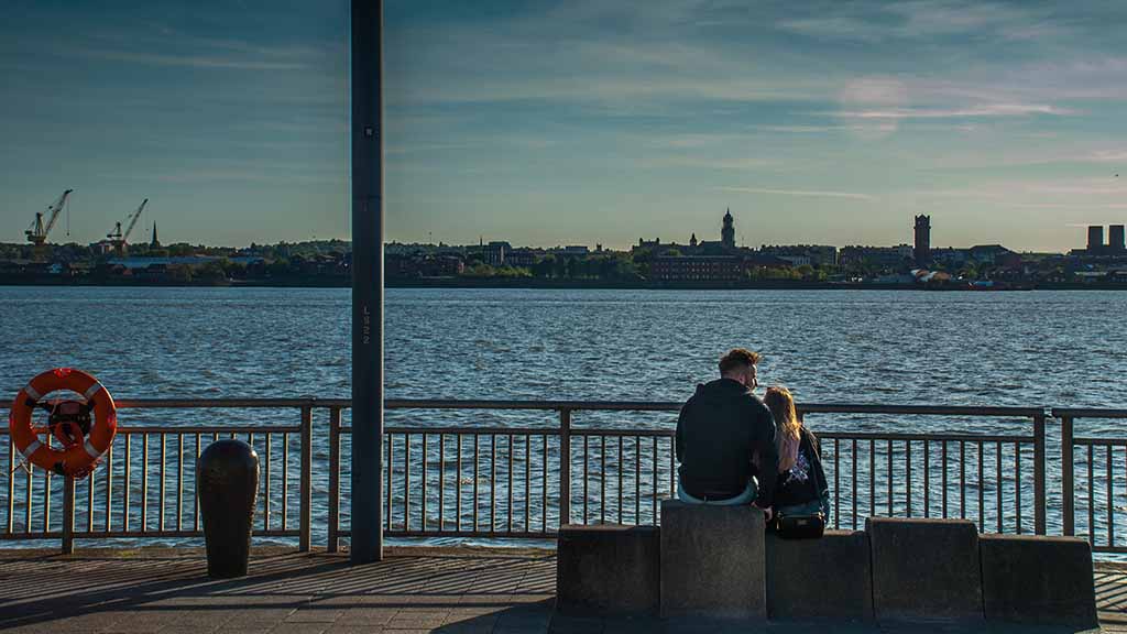 Couple sitting together on a bench cuddling at the edge of the river Mersey