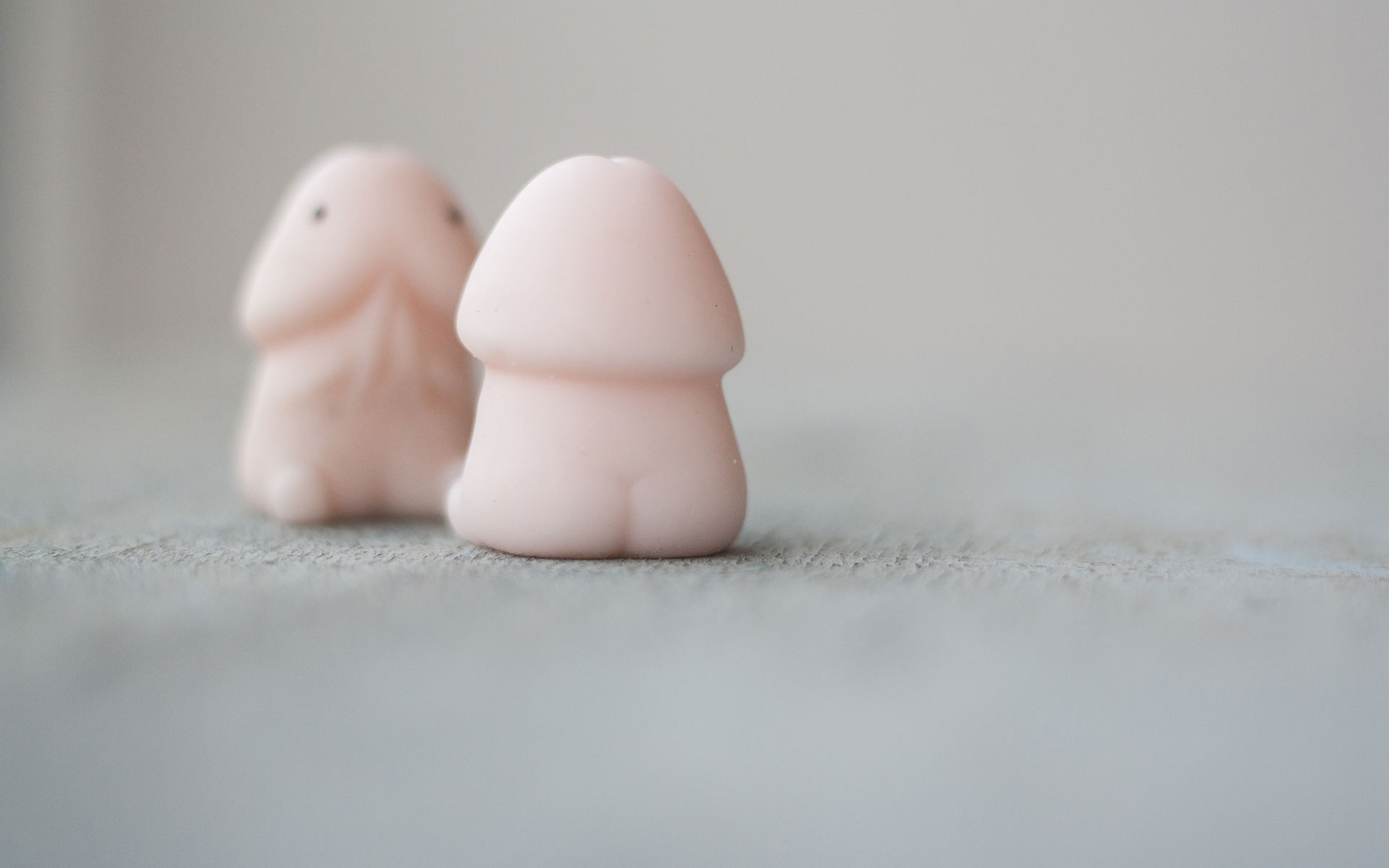 Wax character in the shape of a penis sitting down and looking at its reflection in front of a mirror.