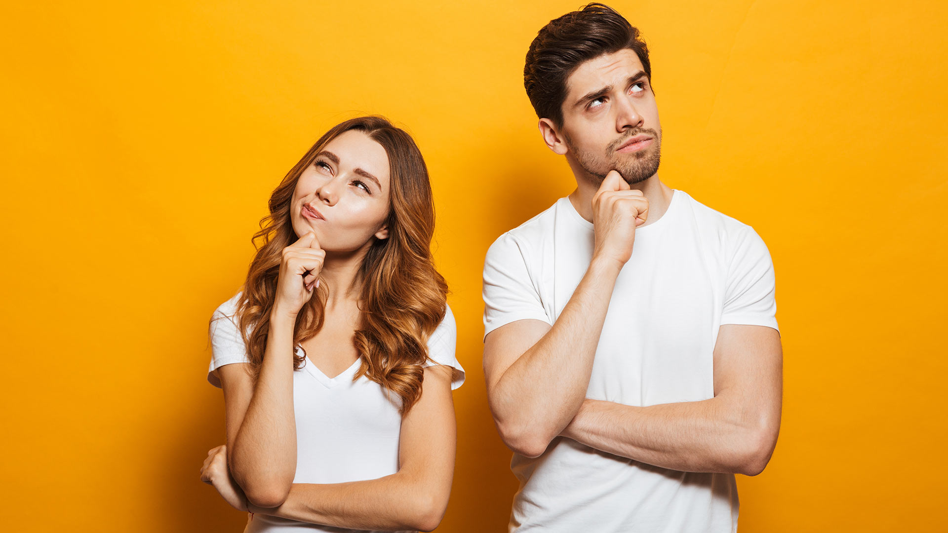 Brunette man and woman in white t-shirts rubbing their chins while deep in thought. Orange background behind them.